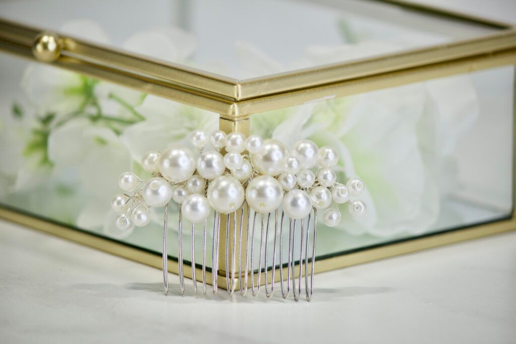 Pearl hair comb in front of a gold-framed glass box with white flowers.