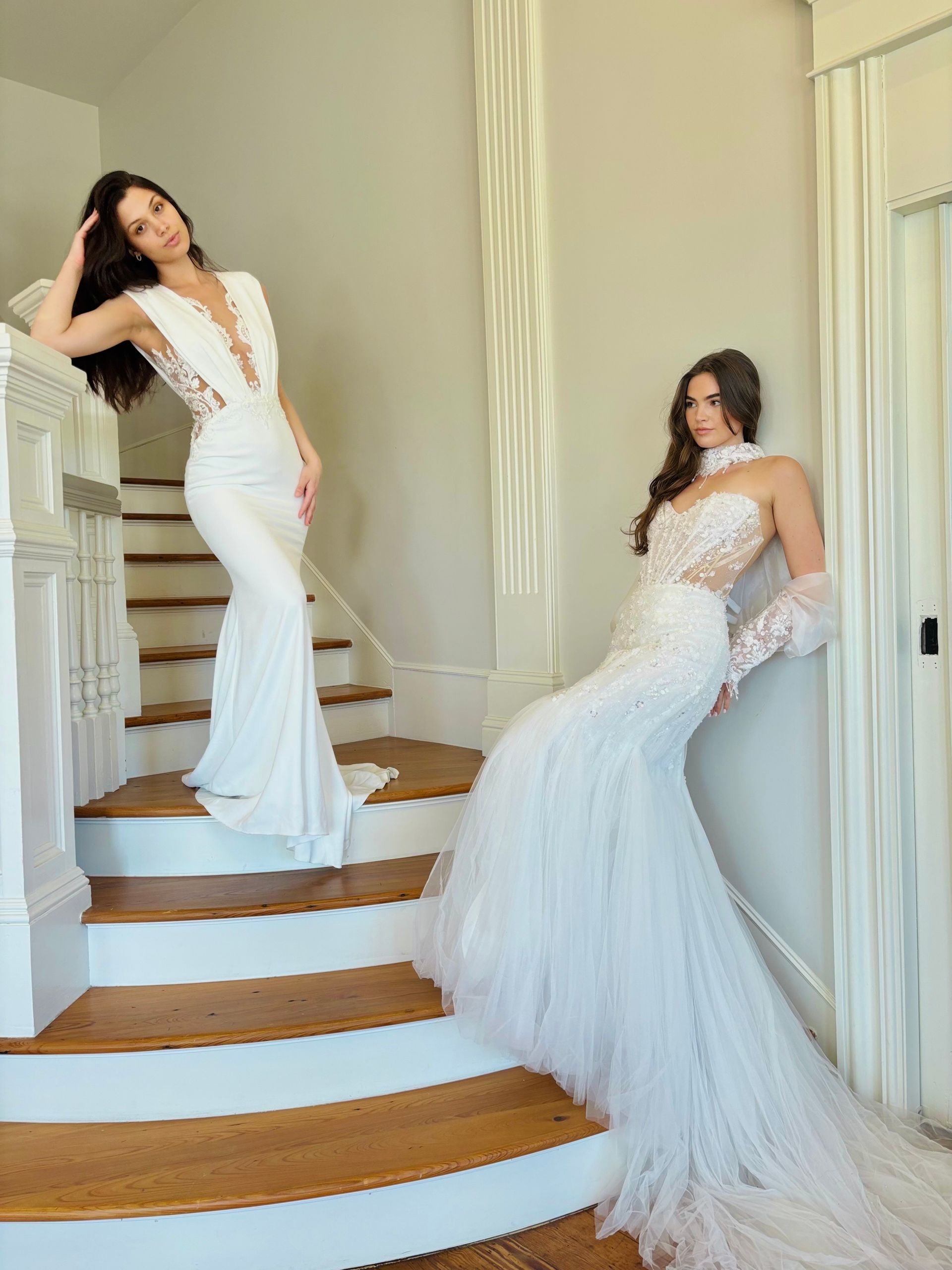 Woman in a white wedding gown with feather skirt, posing outdoors near a stone wall and walkway.