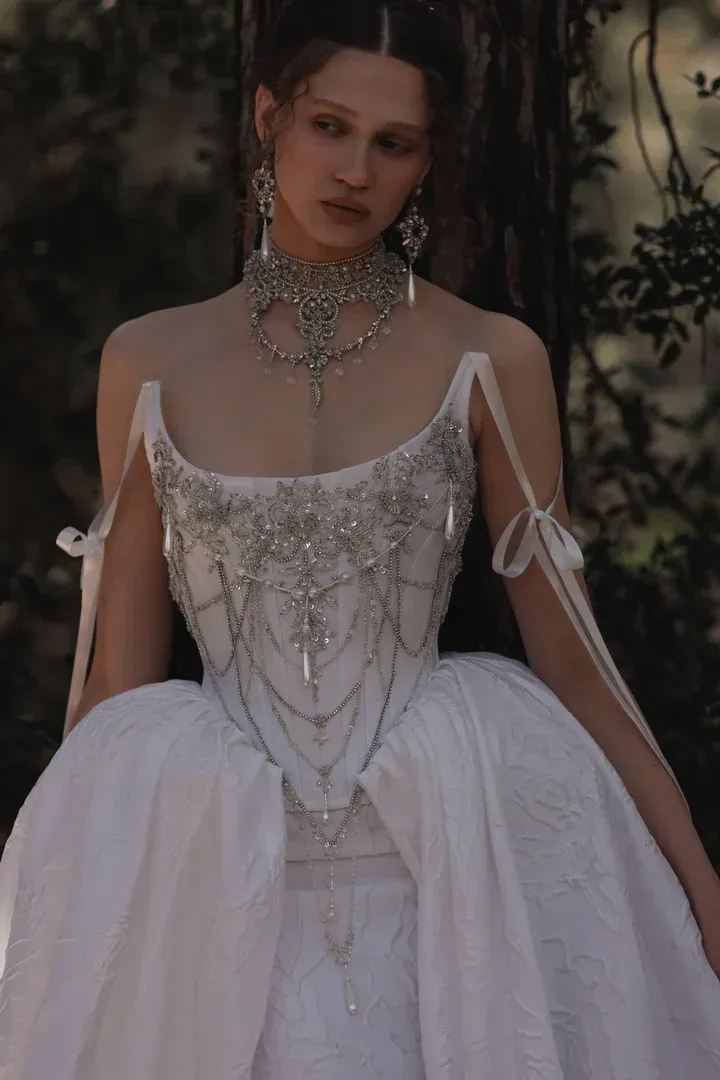 Woman in a white corset wedding dress with lace details and elaborate cross jewelry.