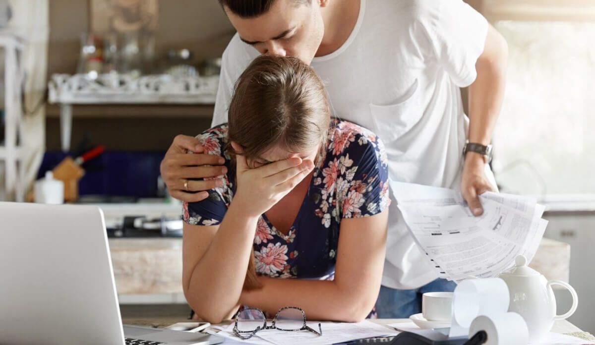 A man is kissing a woman on the forehead while she looks at her laptop.
