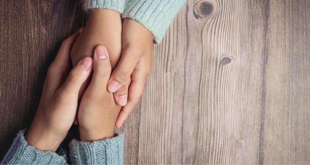 Two people are holding hands on a wooden table.