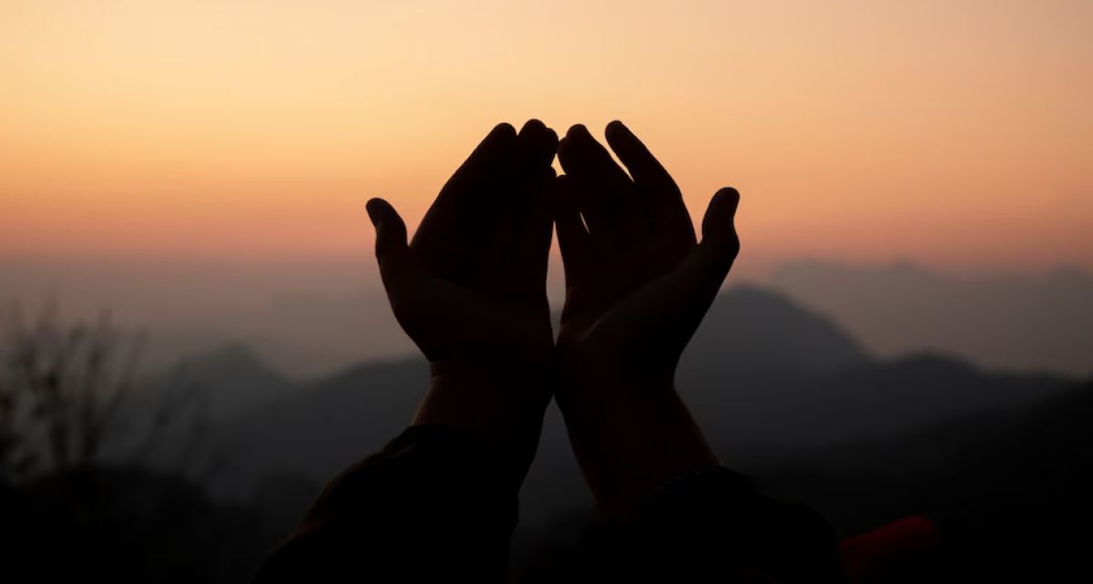 A person is praying with their hands in the air at sunset.
