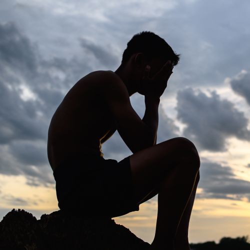 A silhouette of a man sitting on a rock with his head in his hands