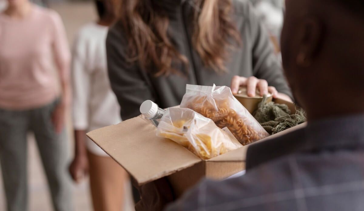 A woman is giving a box of food to a man.