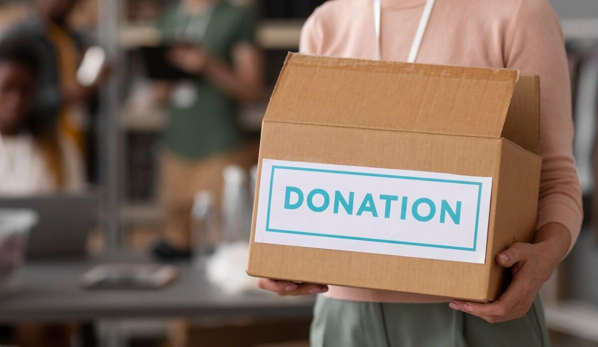 A woman is holding a cardboard box with the word donation on it.