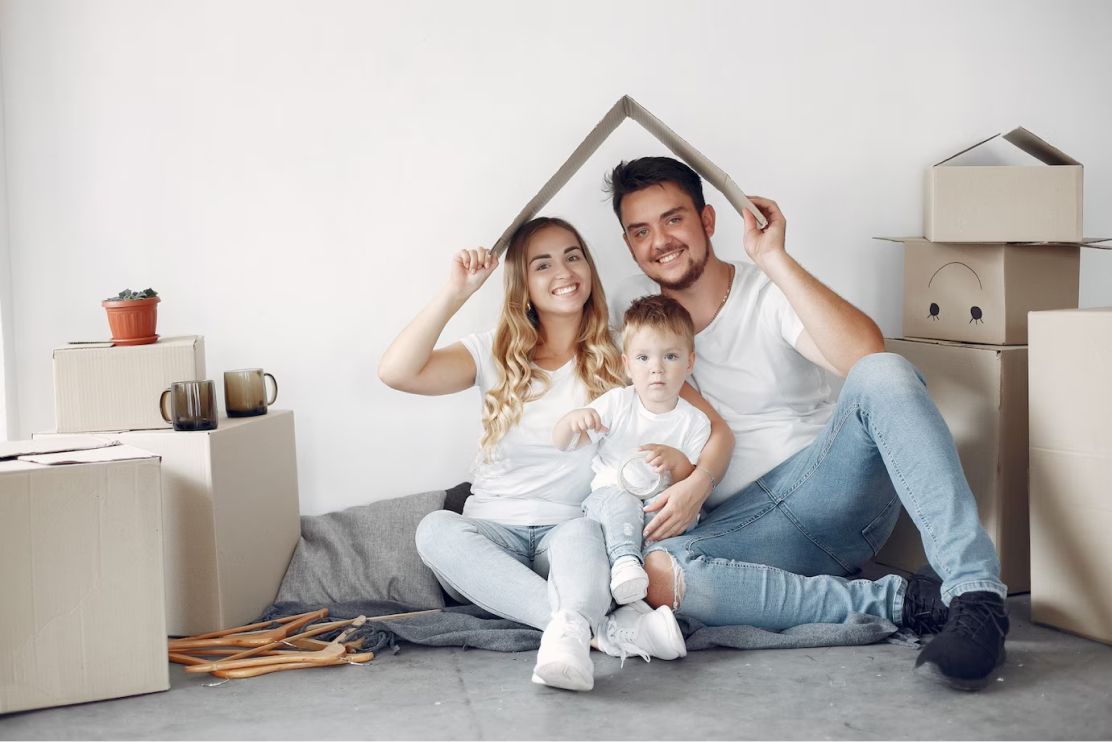 A family is sitting on the floor in their new home holding a cardboard house.