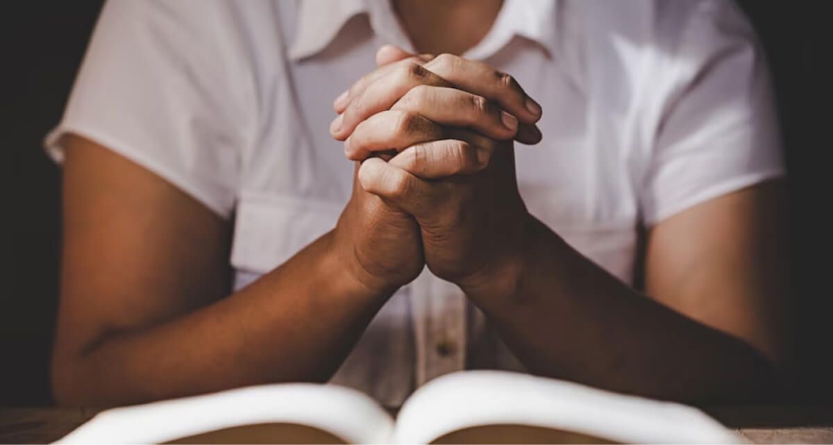 A woman is praying with her hands folded over an open bible.