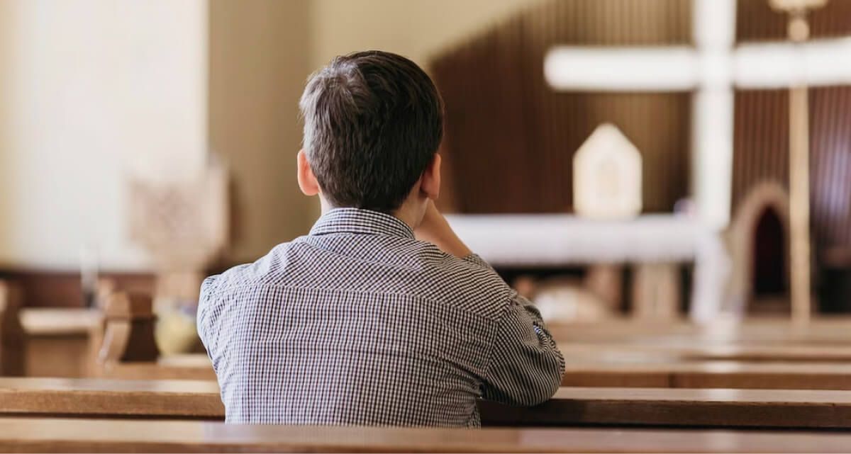 A man is sitting in a church looking at a cross.