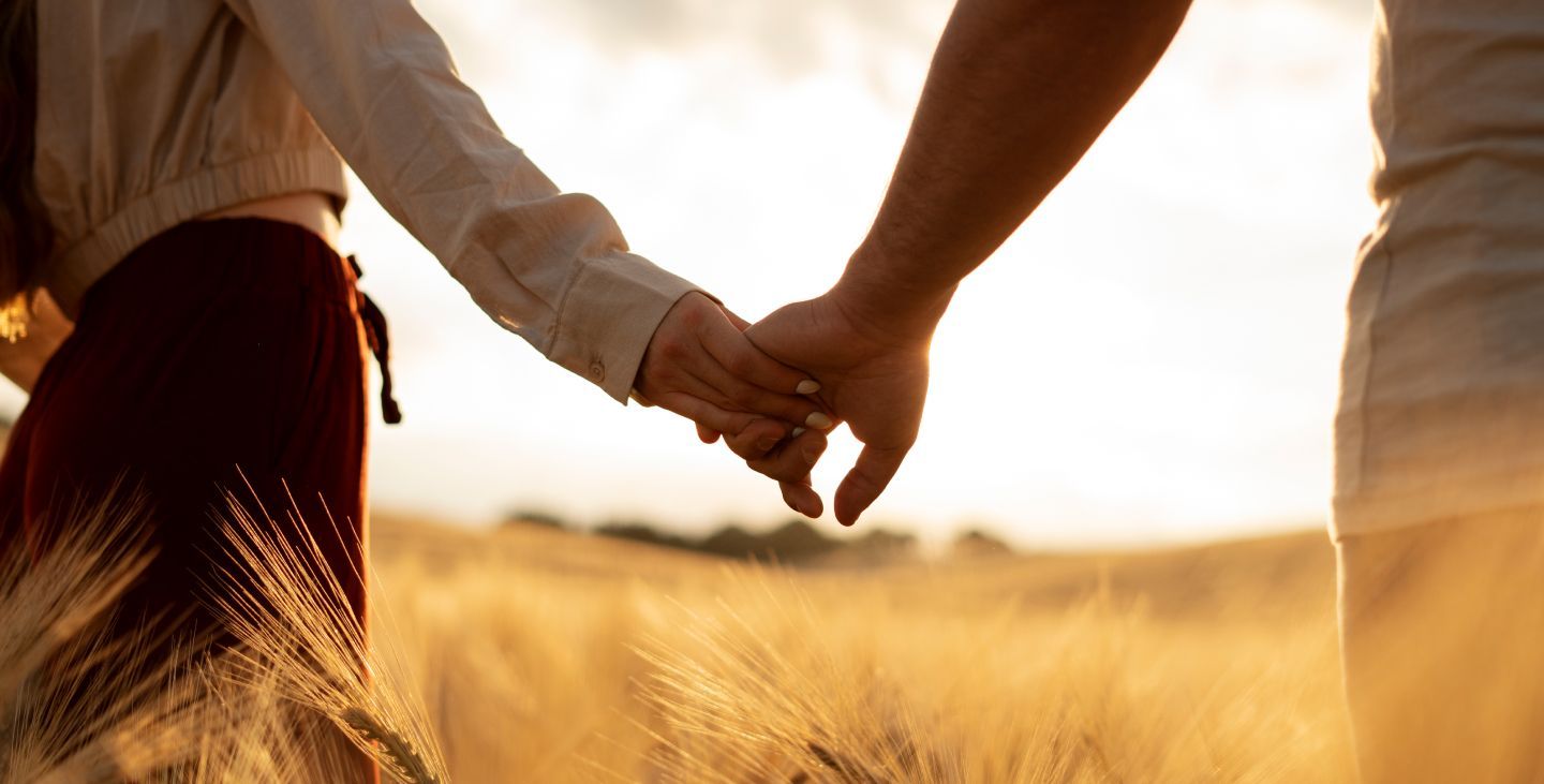 A man and a woman are holding hands in a field of wheat.