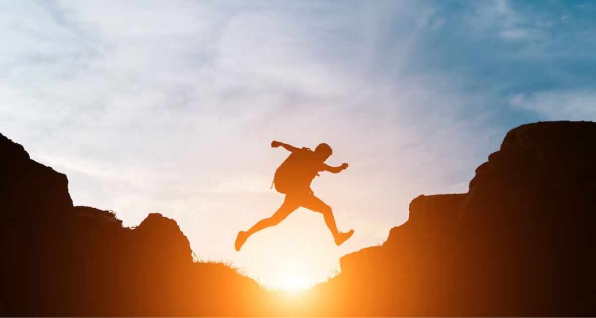 A man is jumping over a cliff at sunset.