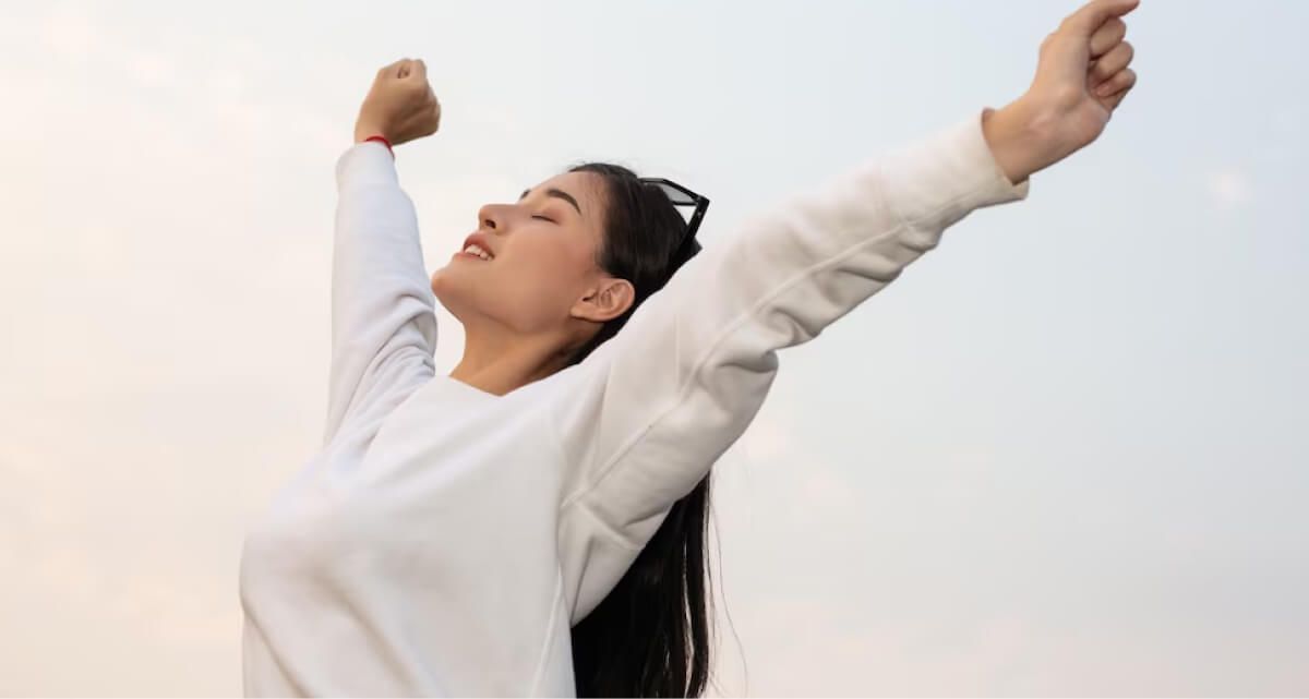 A woman in a white sweater is standing with her arms outstretched.