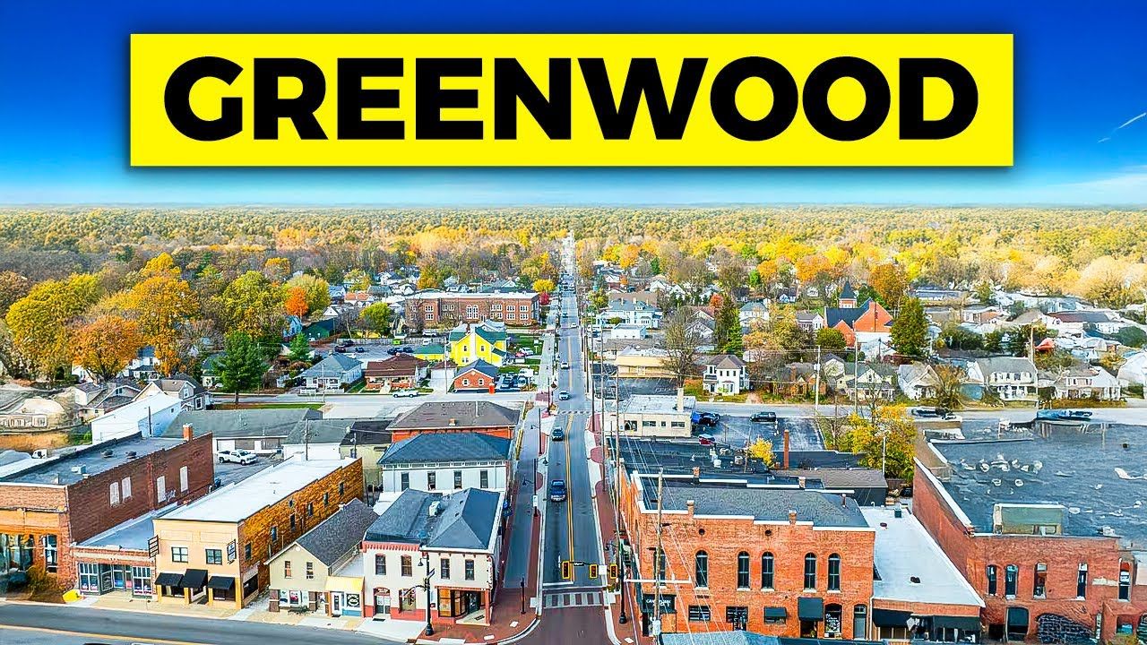 Aerial view of Greenwood, IN, with a street lined with buildings and a yellow banner that reads 