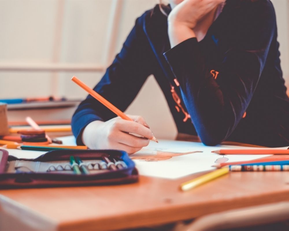 A woman is sitting at a desk writing with a pencil