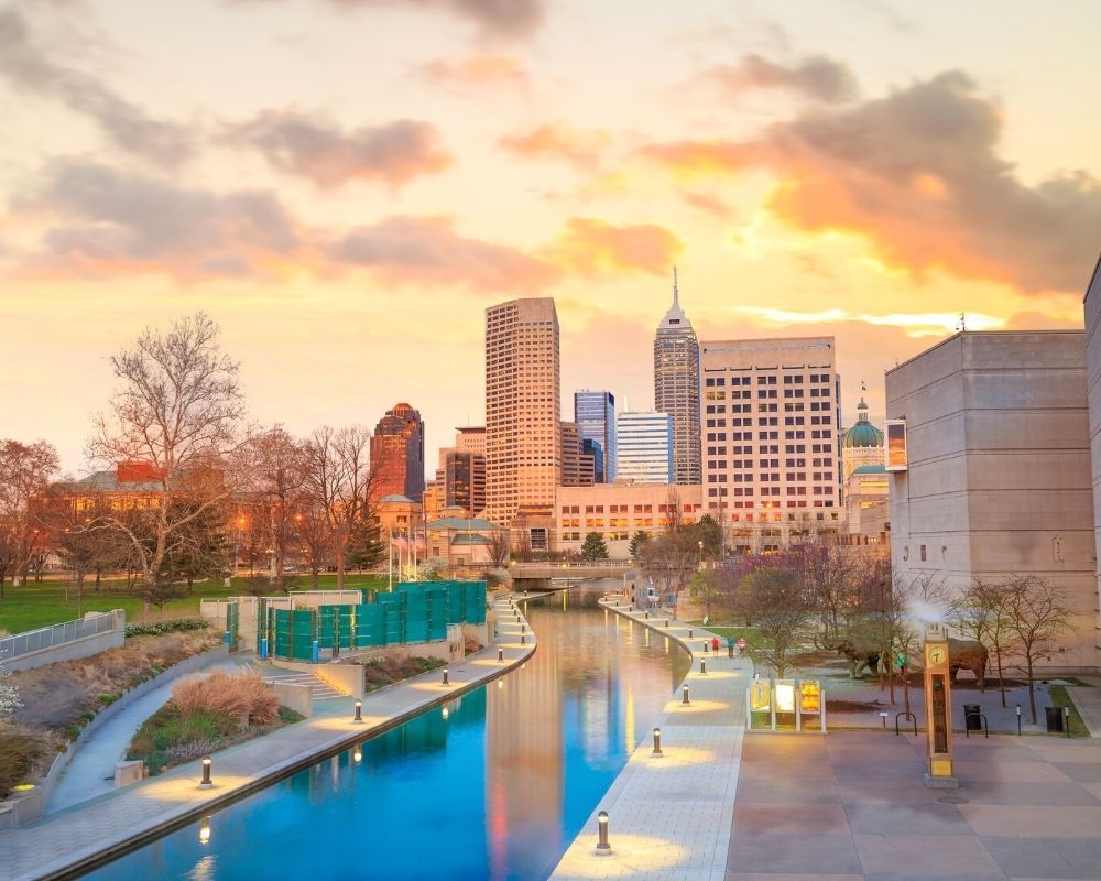 A city skyline with a river in the foreground at sunset.