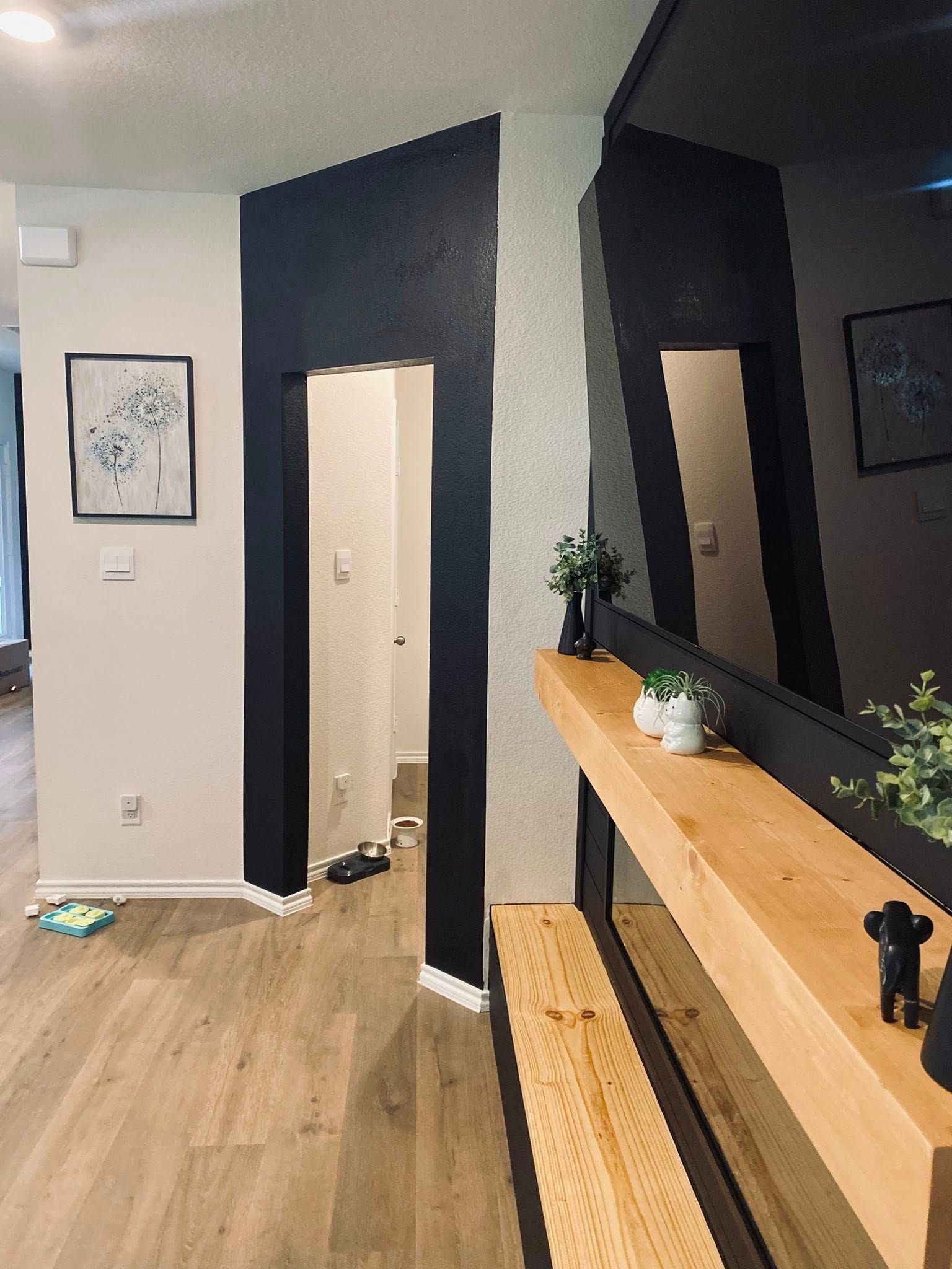 Entryway with black accent walls, wooden console, framed art, and plants.