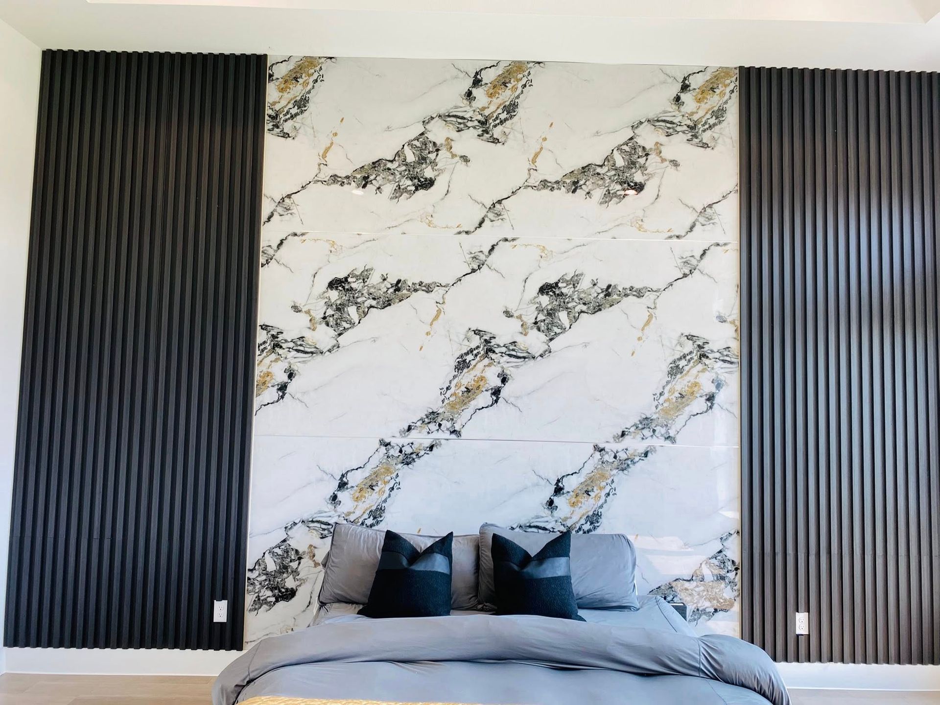 Bedroom with marble accent wall, dark gray ribbed panels, and gray bedding.