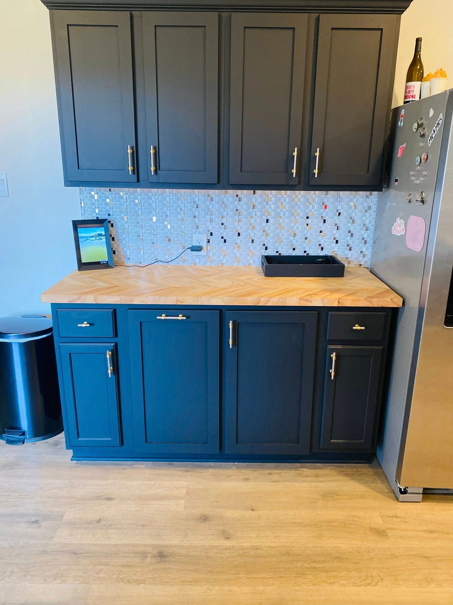 Dark blue kitchen cabinets with light countertops and a stainless steel refrigerator.