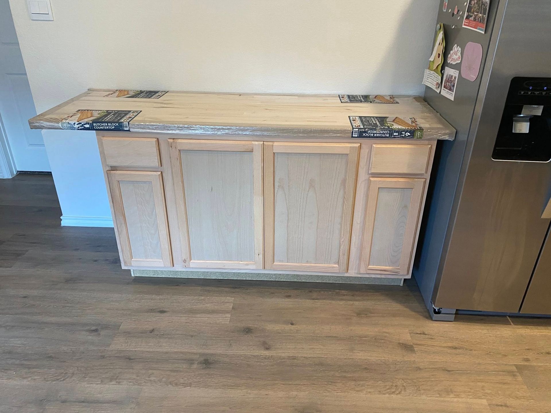 Light wood kitchen island against a white wall and a stainless steel refrigerator.