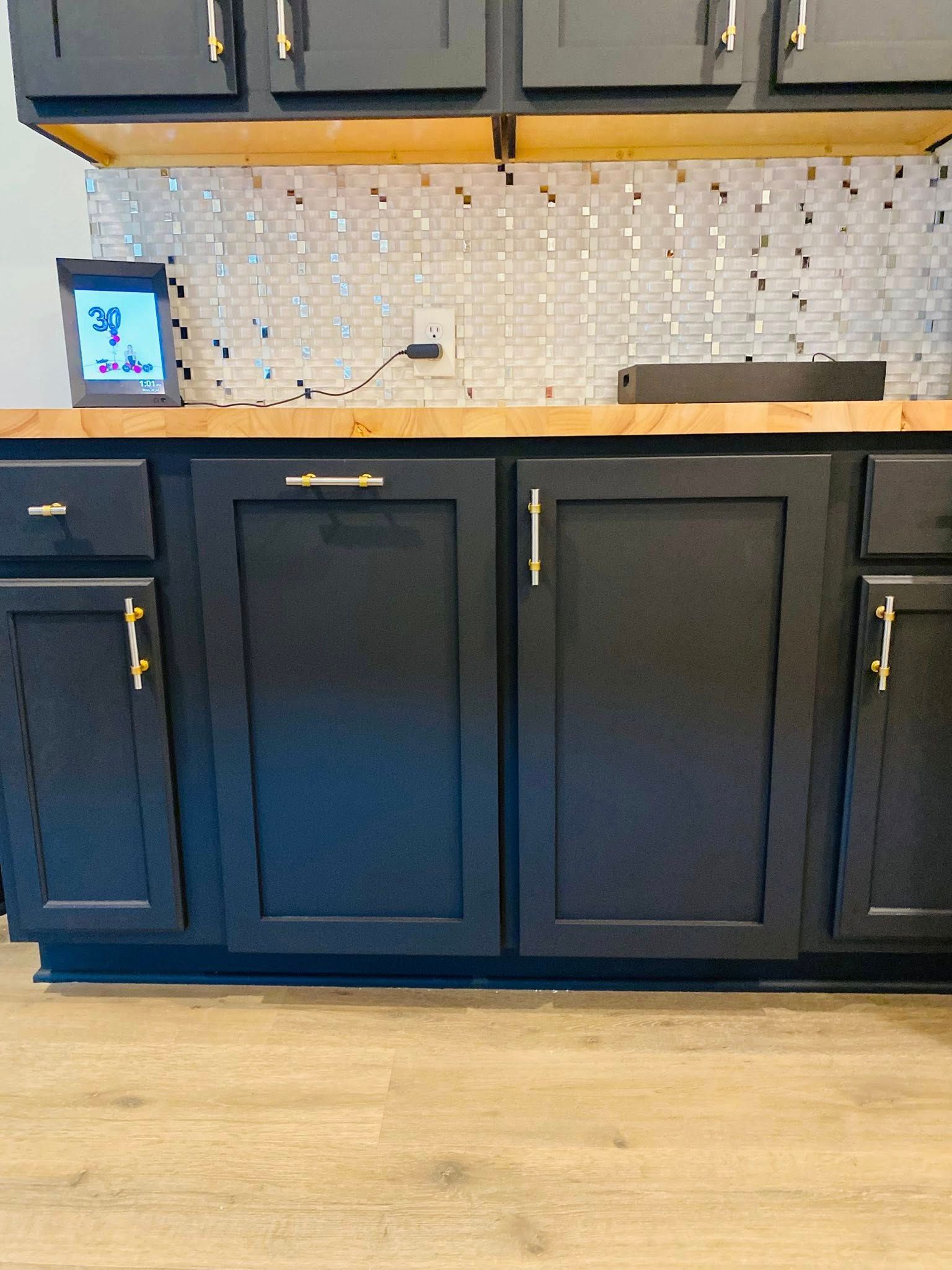 Black kitchen cabinets with gold hardware and a wood countertop.