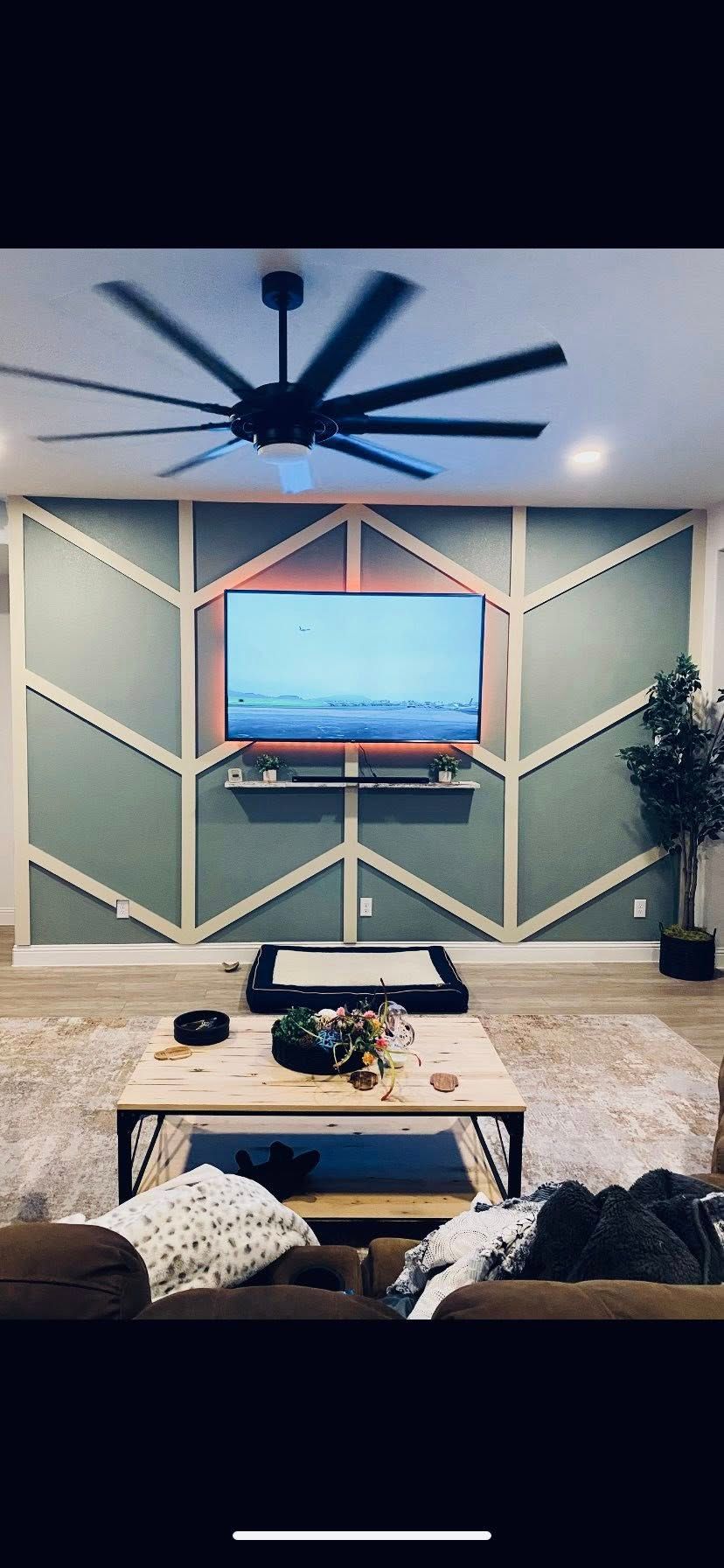 Living room with TV on a geometric wall. A large ceiling fan and coffee table are in the space.