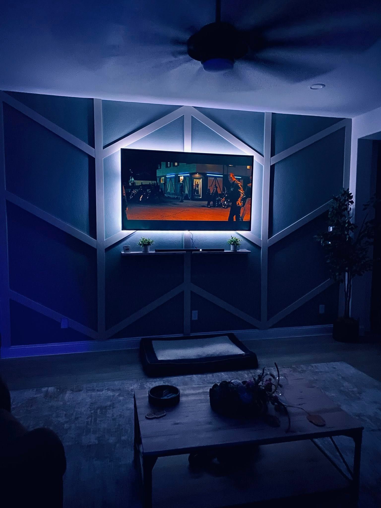 Living room with geometric accent wall, TV, and blue LED lighting.