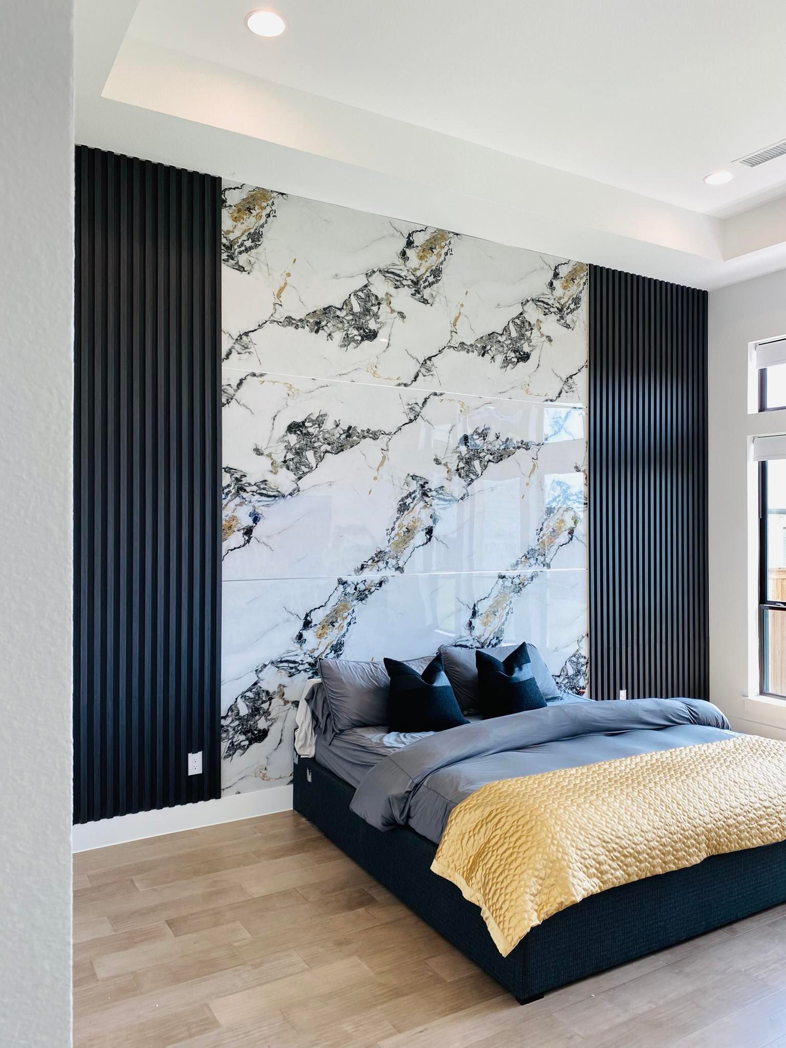 Bedroom with marble accent wall, black ribbed panels, and a gray bed with gold blanket.