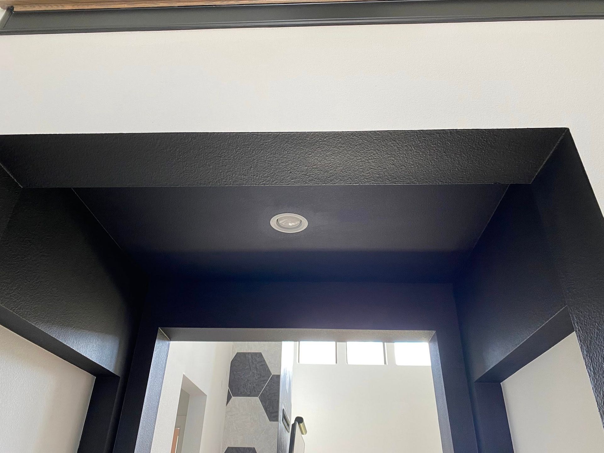 Black painted doorway with recessed ceiling light, viewed from below. White walls contrast the black.