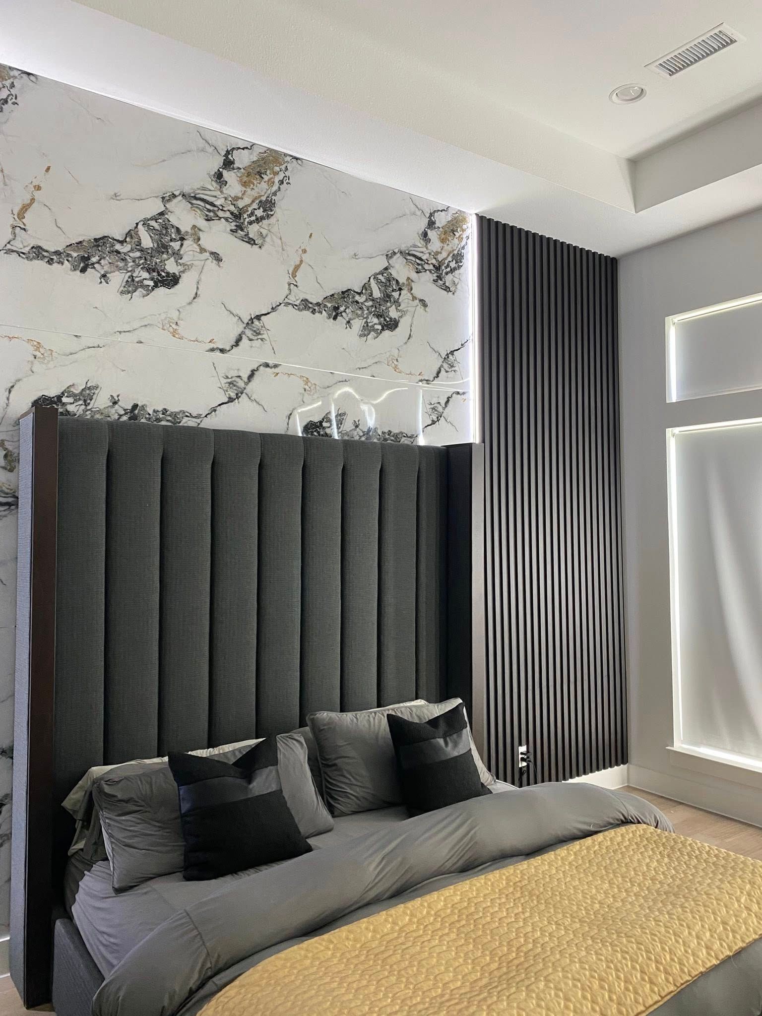 Bedroom with a gray bed, marble-patterned wall, and dark vertical wood paneling.