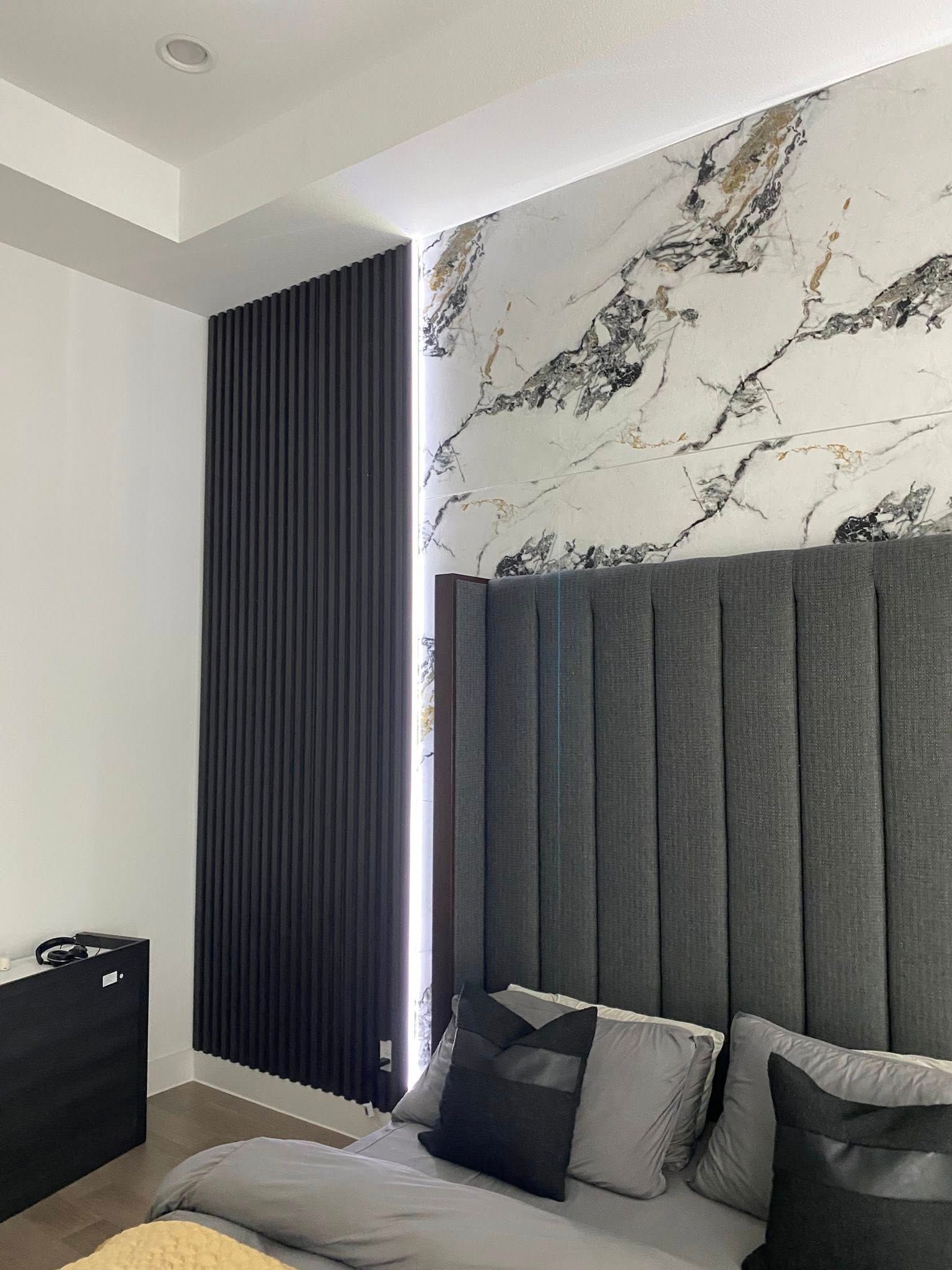 Bedroom with gray headboard, marble accent wall, dark paneling, and bed.