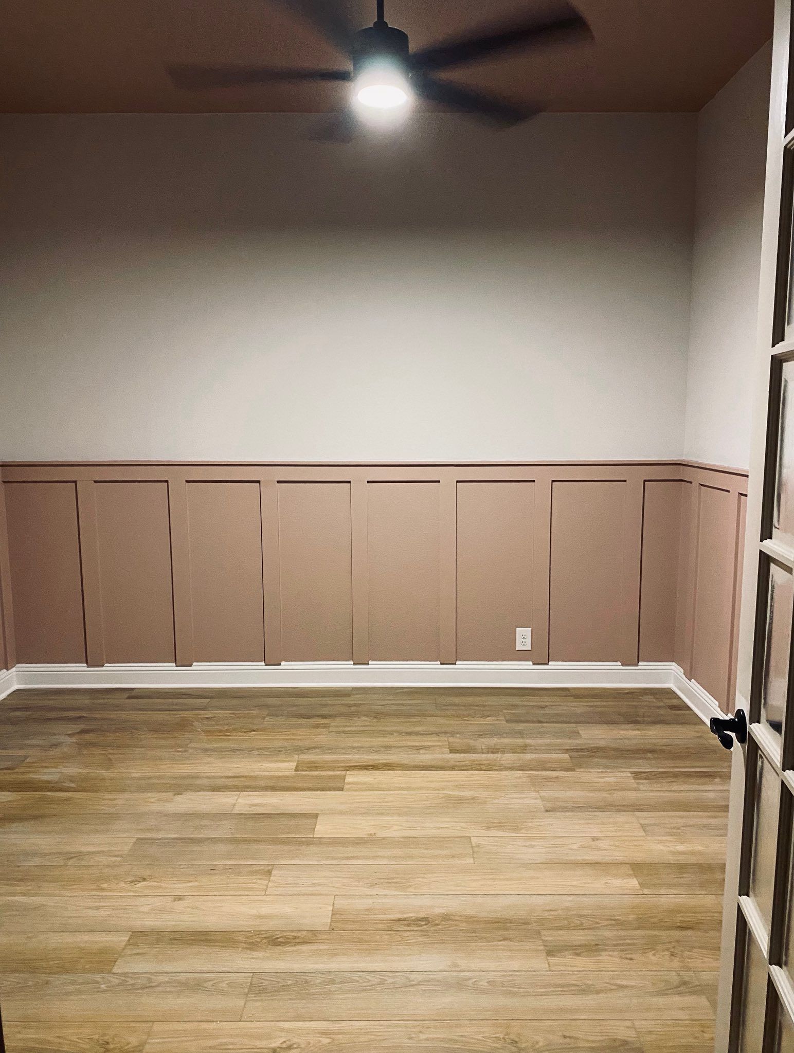 Empty room with light brown wood floor, light pink paneling, white walls, and a ceiling fan.