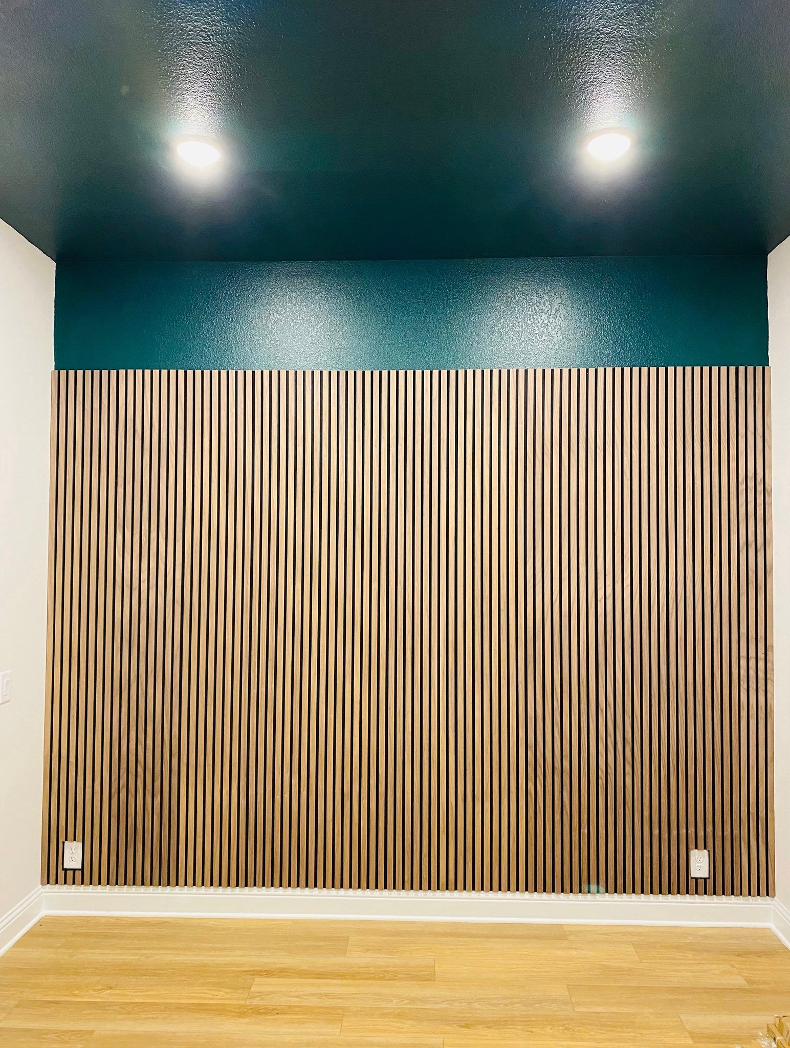 Room with wood-paneled wall, teal and textured ceiling, recessed lights, and light-colored floor.