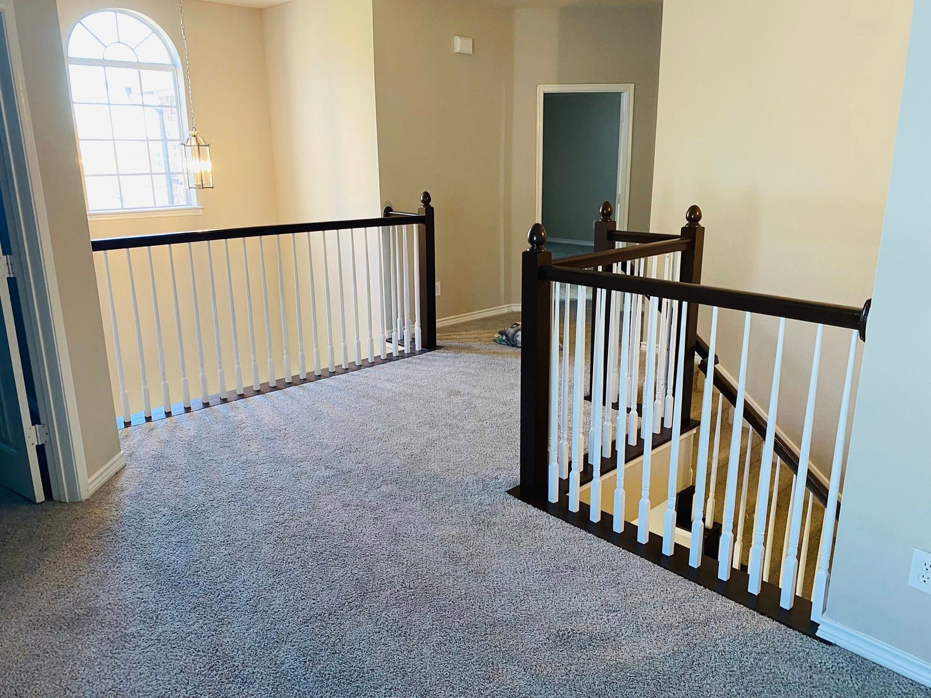 Interior view of a carpeted landing with a staircase and a white railing with a dark wood cap.
