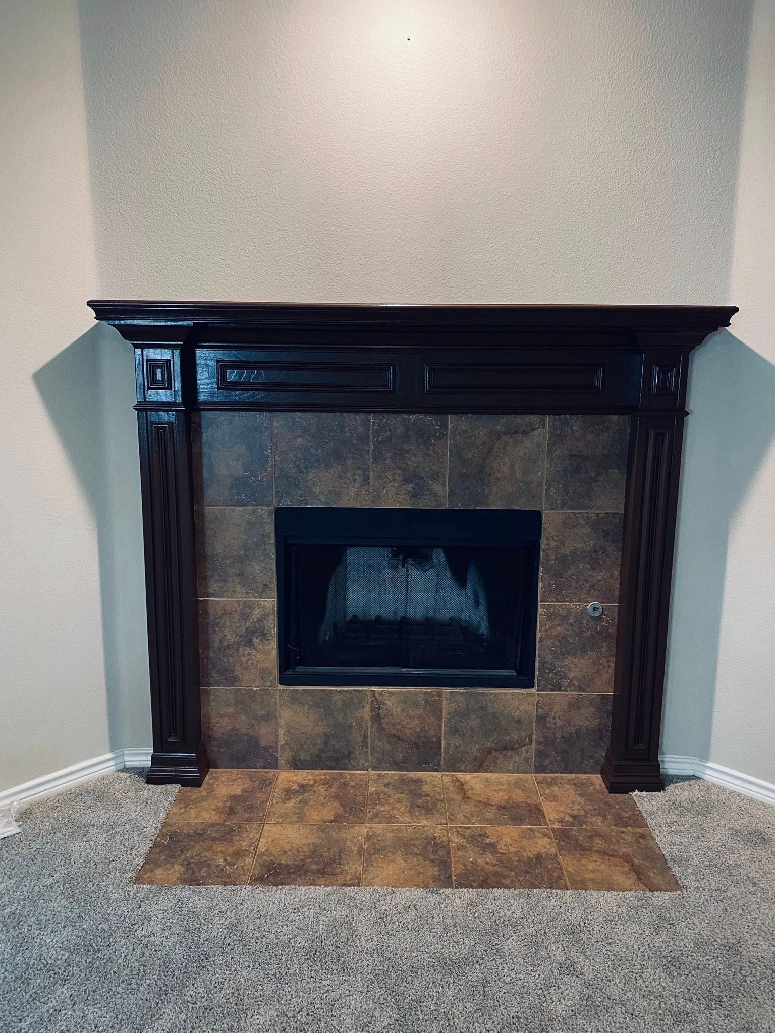 Dark wood fireplace with brown tile surround and hearth, neutral wall, and carpet.