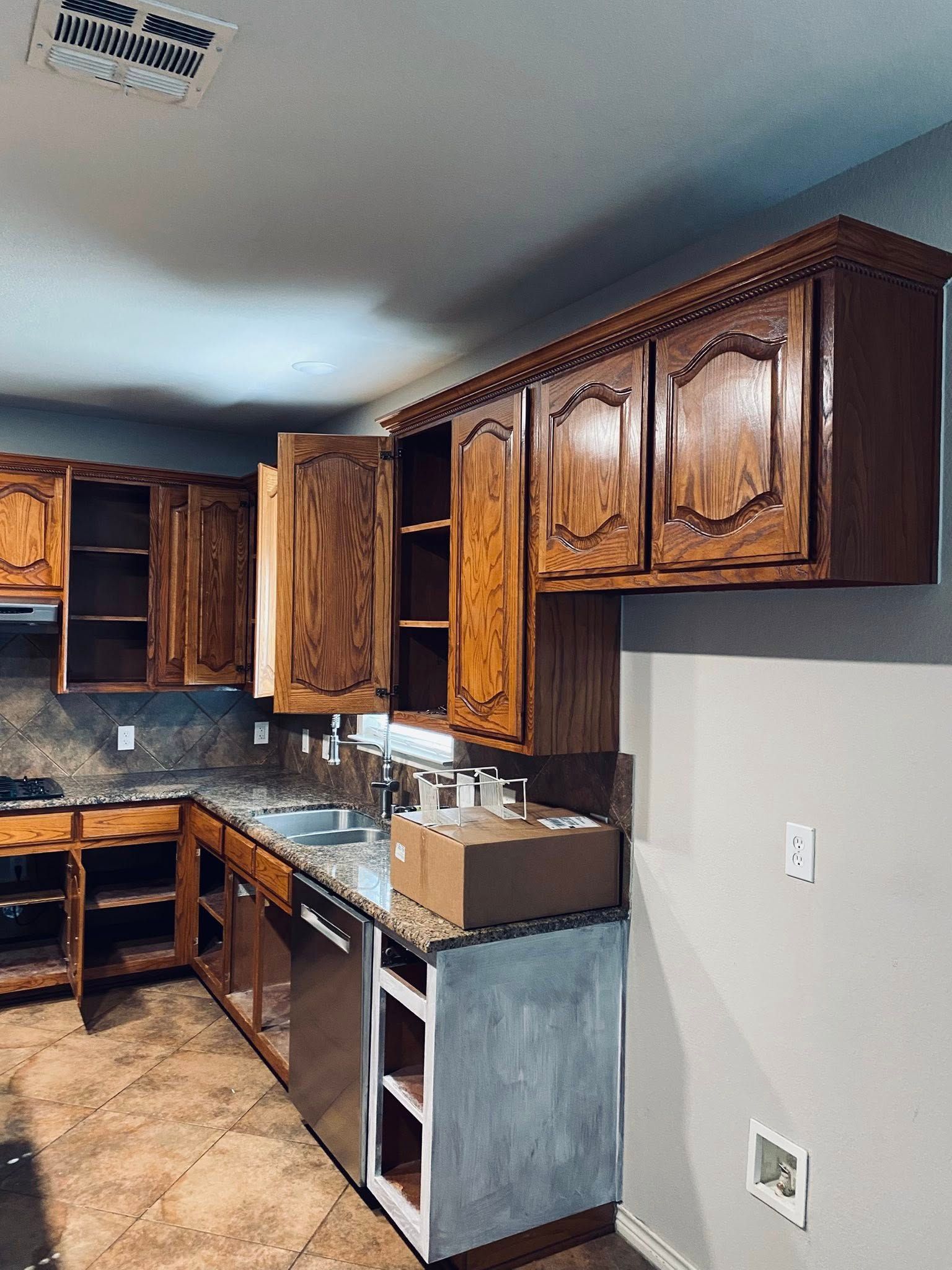 Empty kitchen cabinets; renovation in progress. Brown cabinets, granite countertop, stainless steel sink.