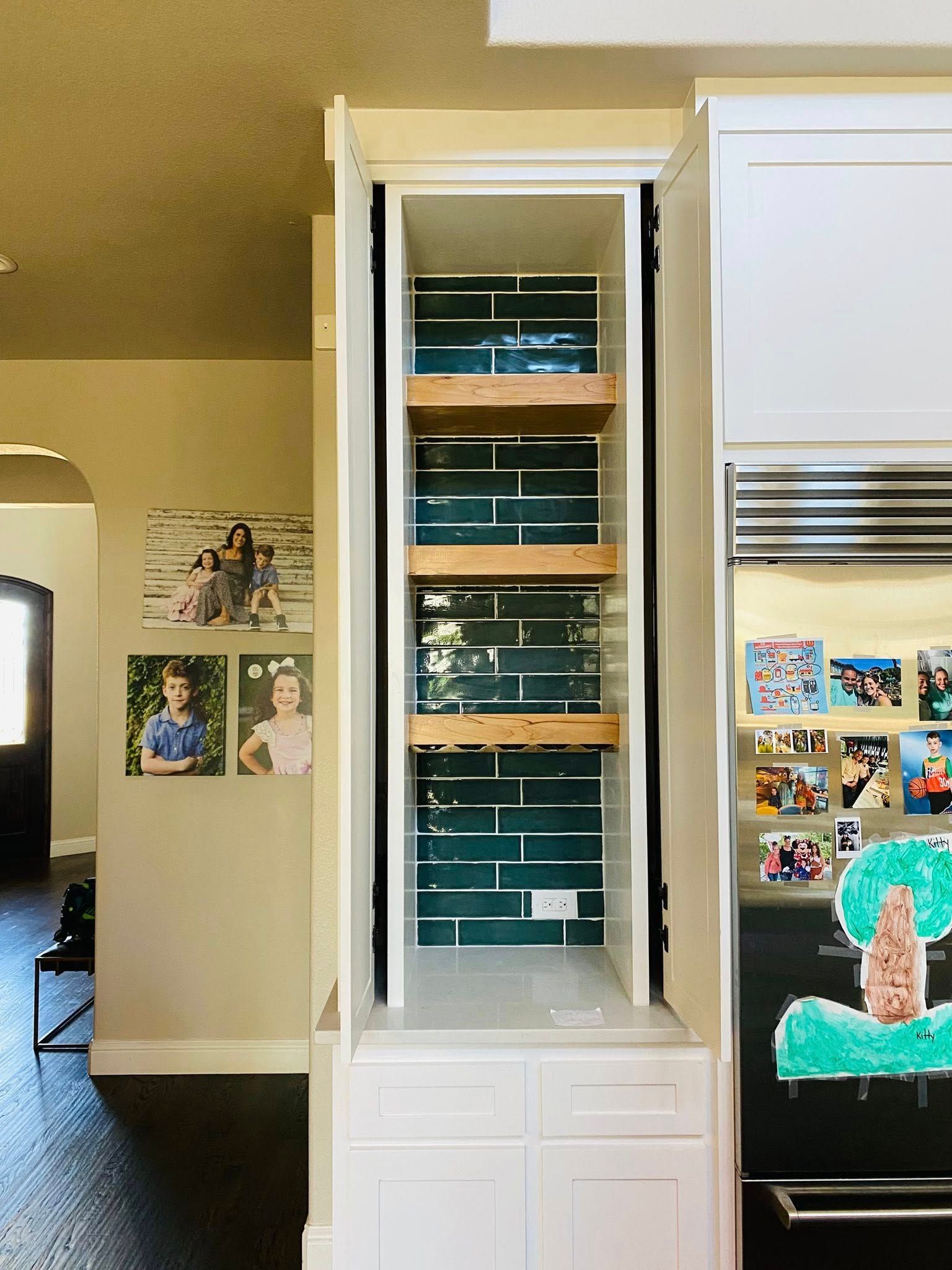 Open pantry with turquoise tile backing and wooden shelves, next to a black refrigerator.
