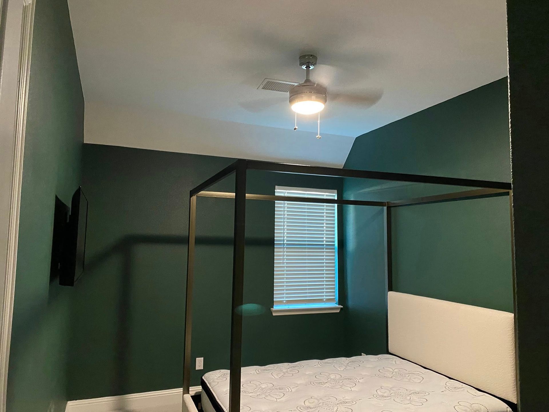 Bedroom with a canopy bed, teal walls, and a ceiling fan.