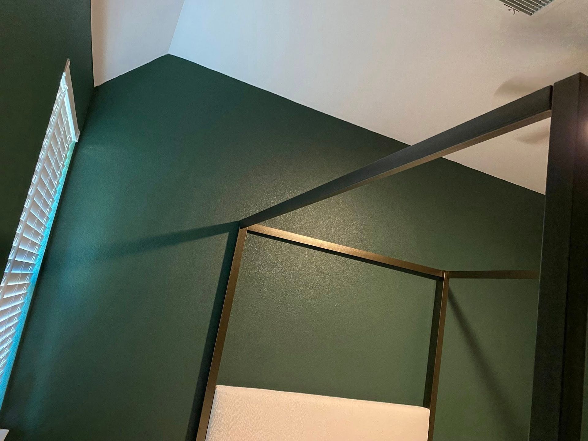 Green wall and white ceiling with a dark metal bed frame and white headboard.