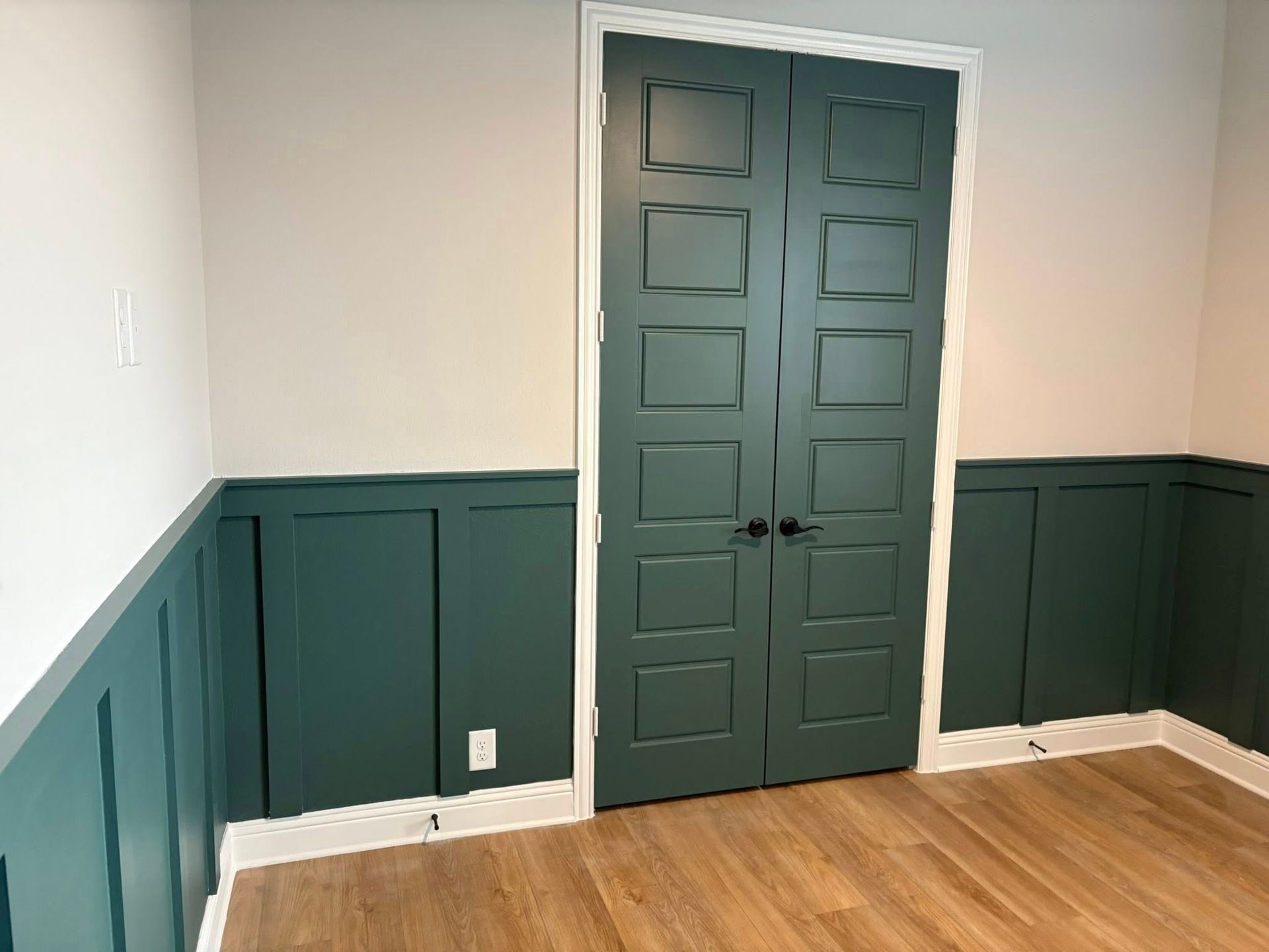 Green paneled walls and matching double doors in a room with light-colored walls and wooden floor.