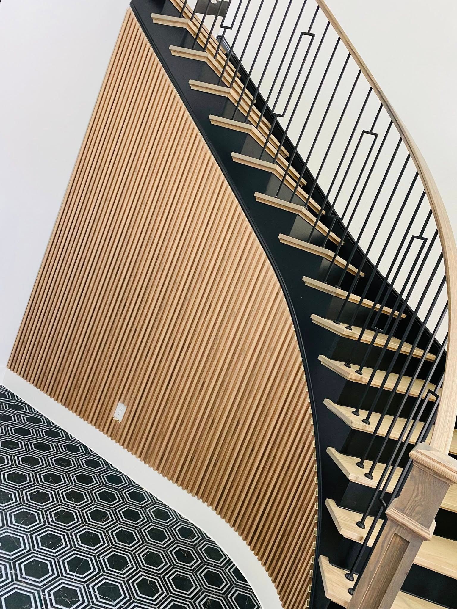 Staircase with wooden panel wall and black and beige steps, black metal railing, and patterned floor.