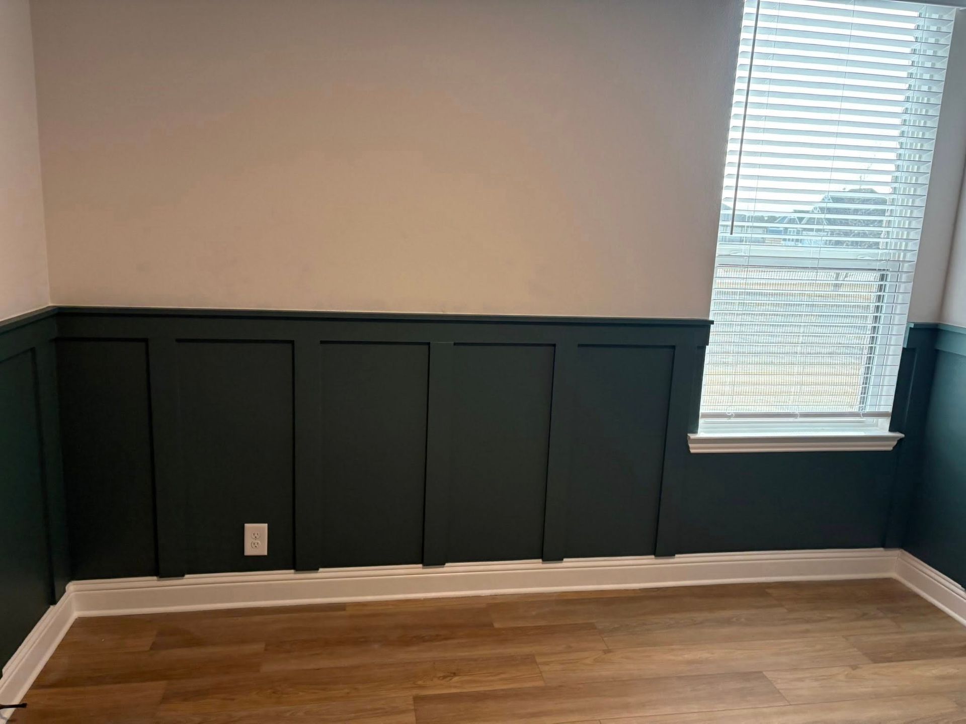 Room with dark green wainscoting and tan upper wall; a window with blinds is on the right.