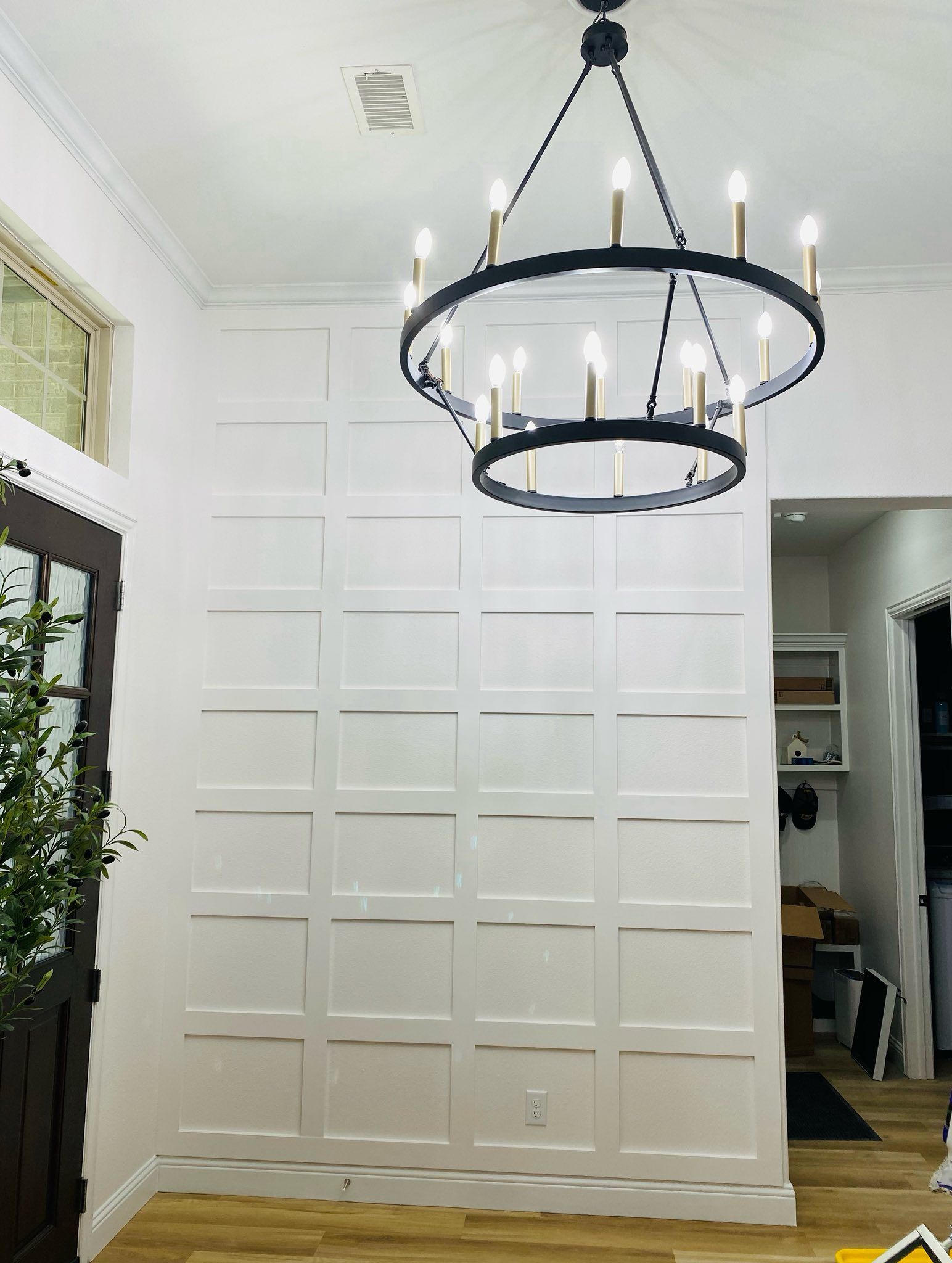 White paneled wall with a black chandelier in an entryway.