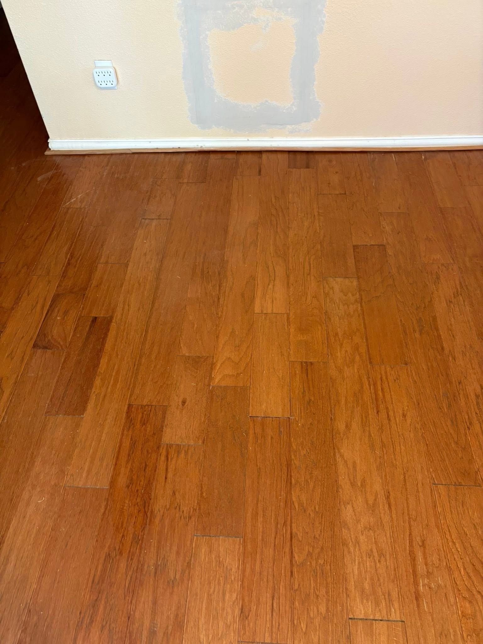 Wooden floor with dust, wall with repaired section and electrical outlet.