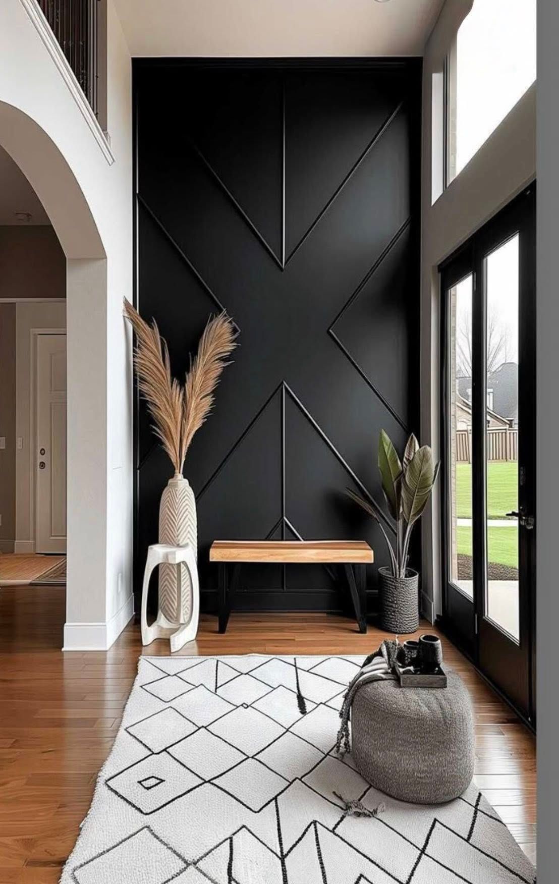 Black accent wall with geometric design, bench, rug, decorative plants, and large window.