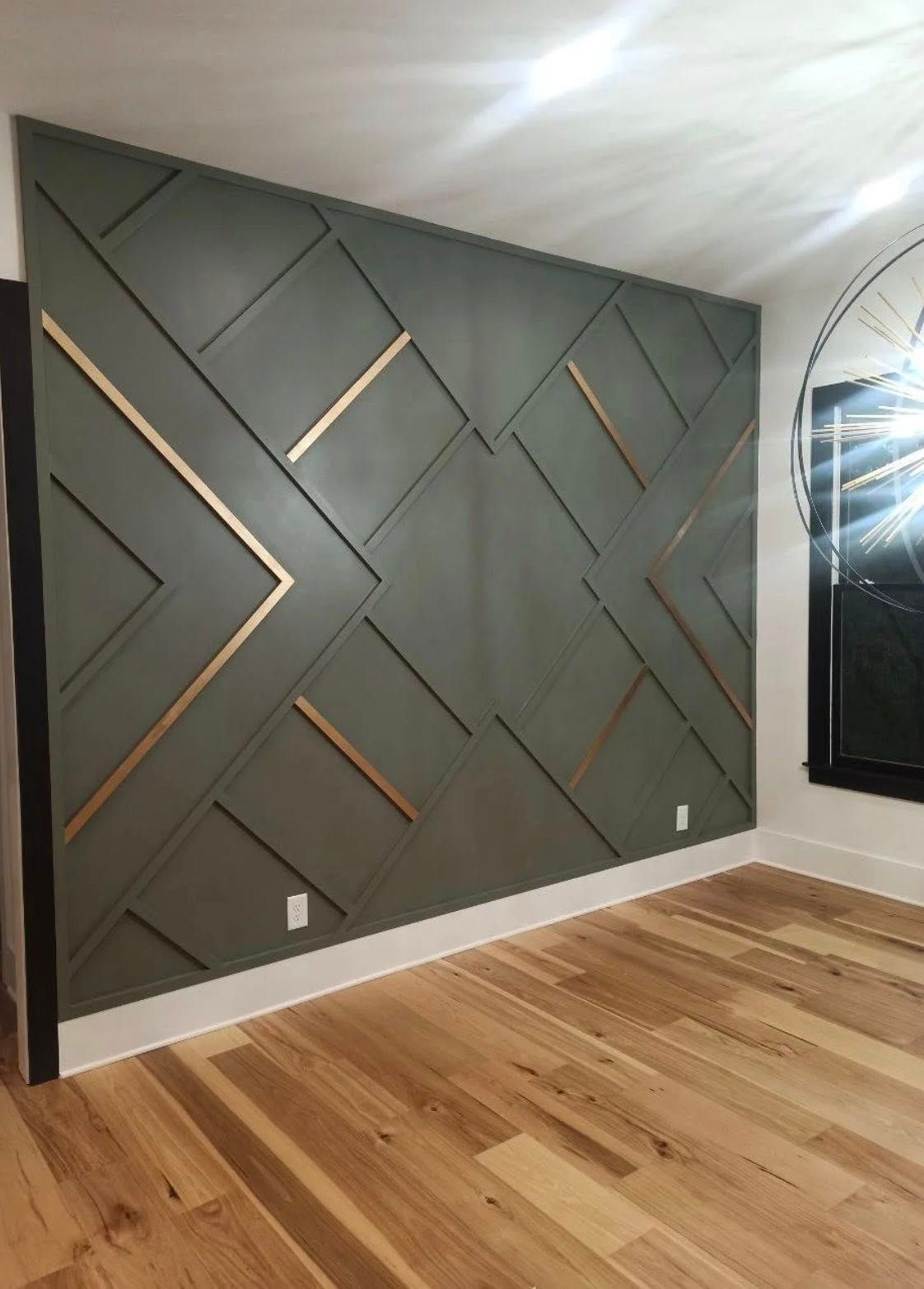 Green geometric accent wall with gold accents in a room with hardwood floors and white trim.