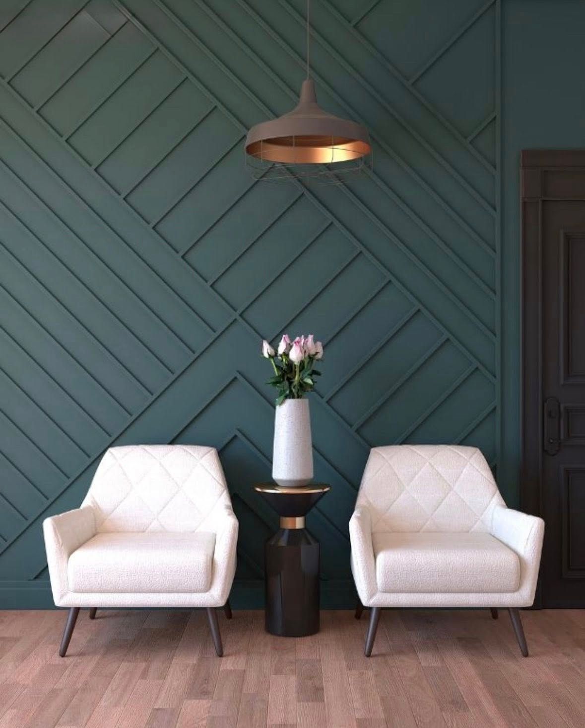 Two white armchairs face a table with flowers, against a teal paneled wall. A light hangs overhead.