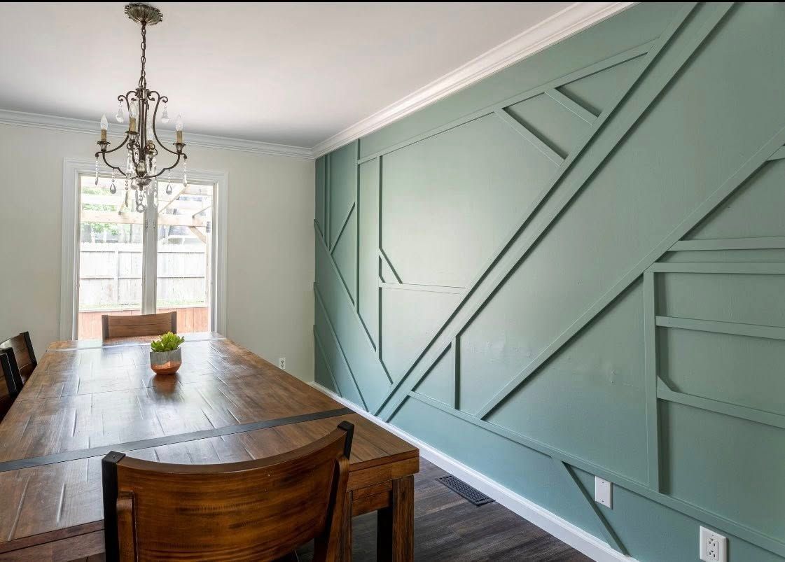 Dining room with aqua accent wall with geometric molding, wood table, chandelier.