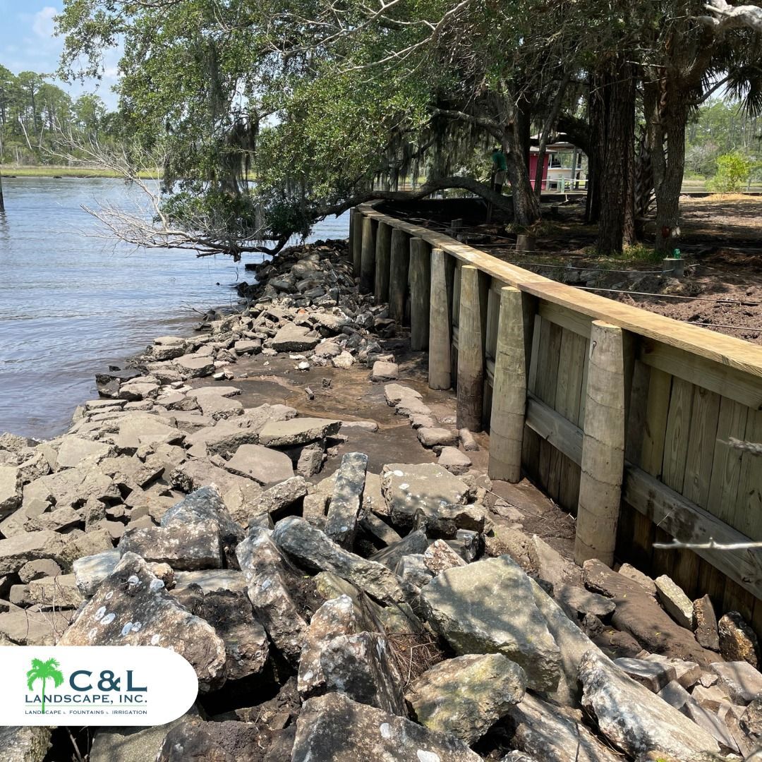 A wooden sea wall along a rocky shoreline with trees in the background.