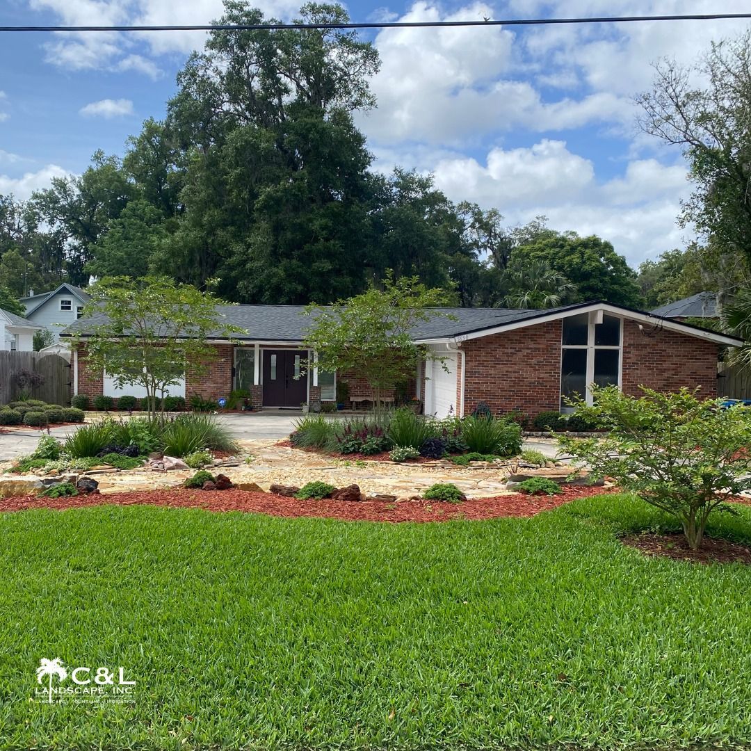 A single-story brick house with landscaping. Trees and grass in the yard, a blue sky overhead.