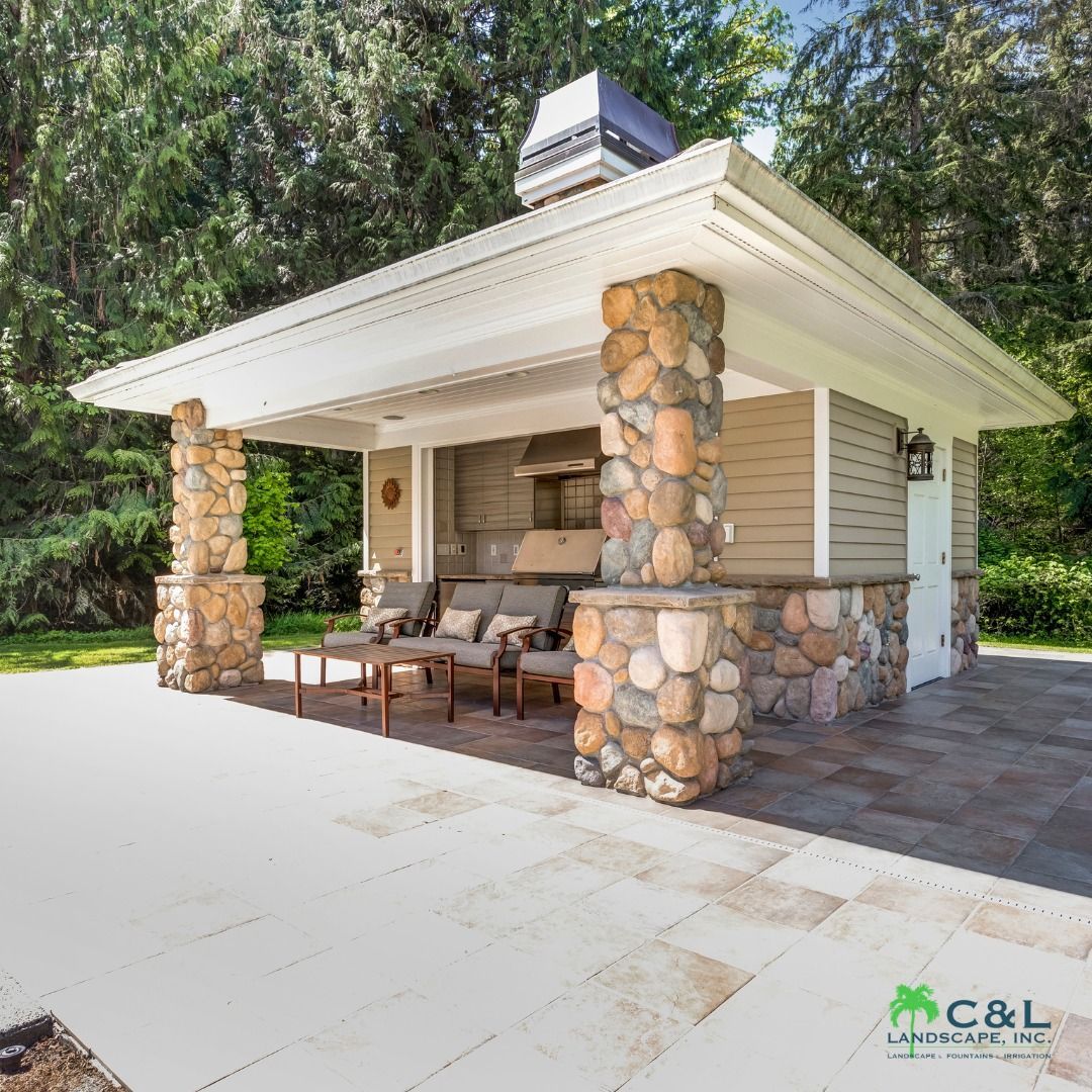 Outdoor kitchen with stone columns, built-in grill, seating area, and light tan siding.