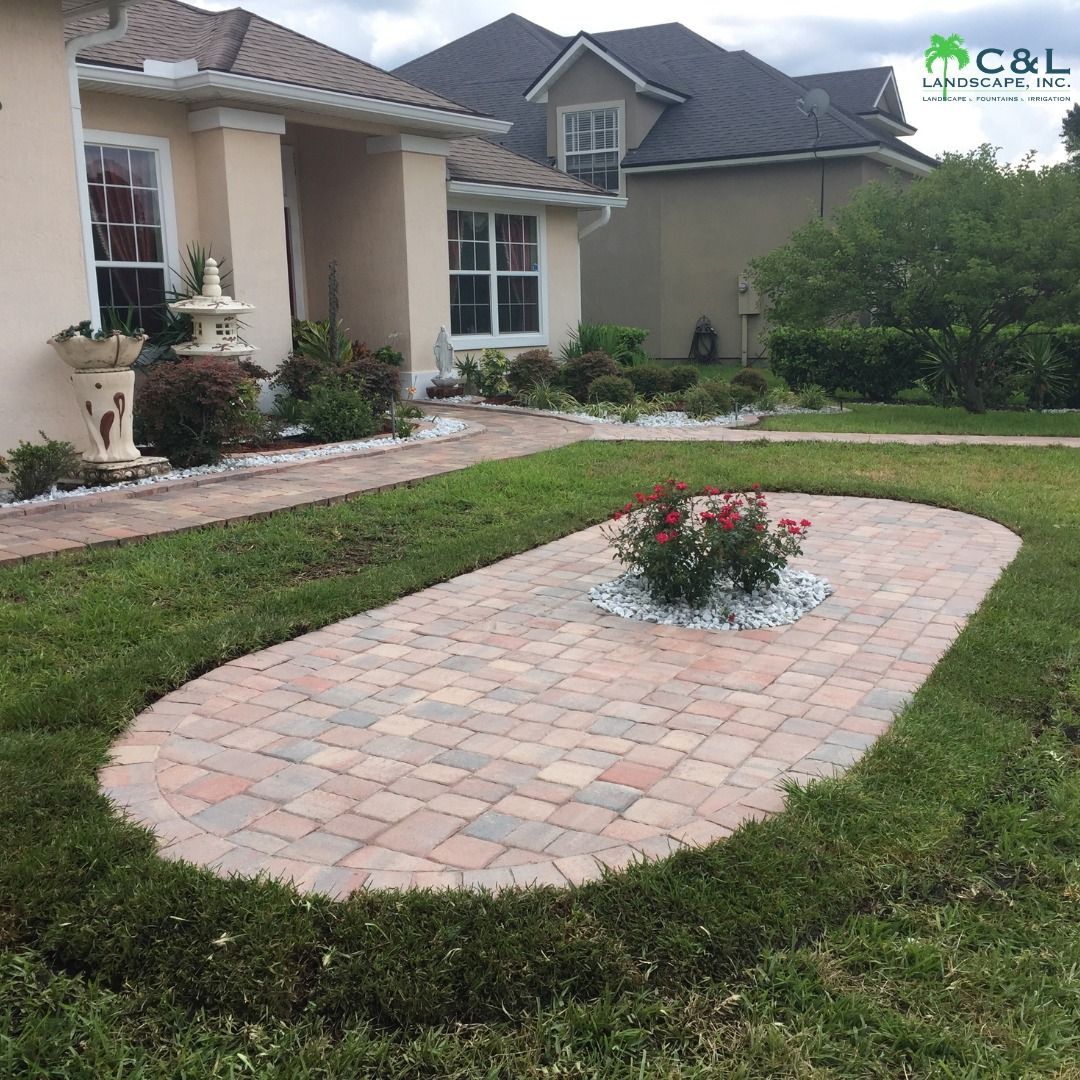 Paver patio with rose bush surrounded by white stones, in front of a house.